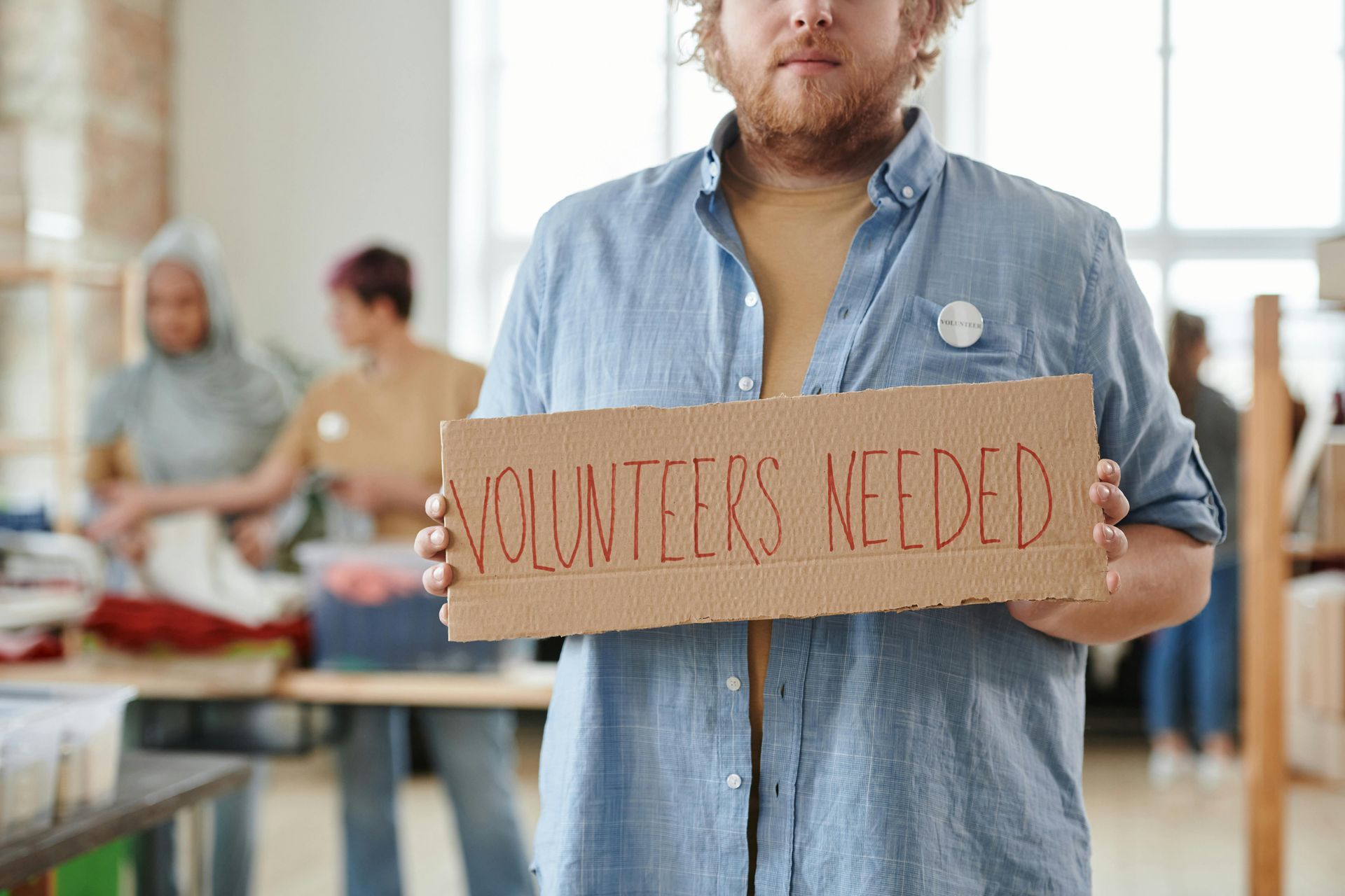Man holding a volunteers needed sign
