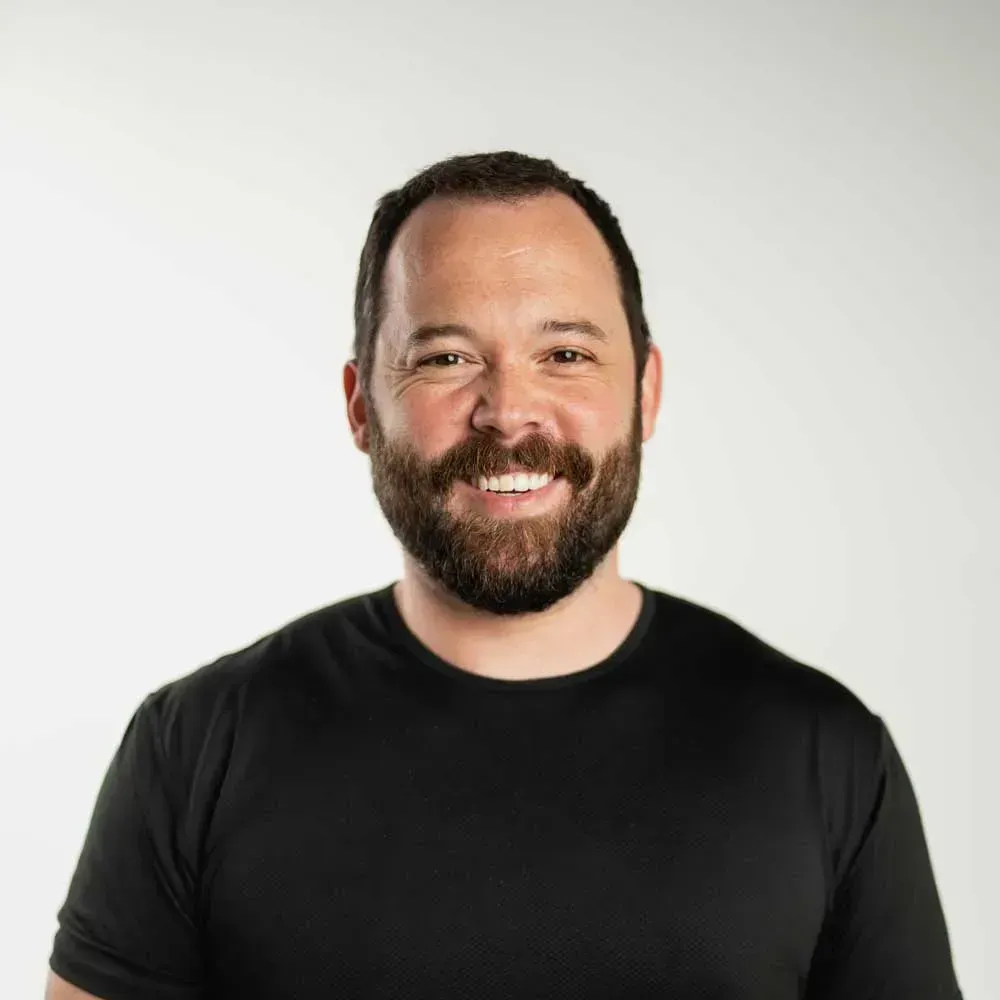 A man with a beard is wearing a black shirt and smiling.