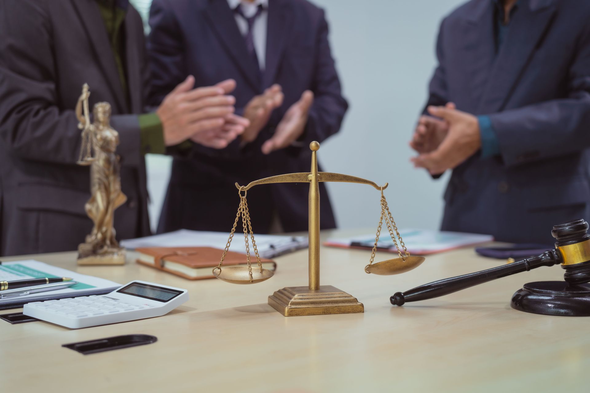 Three lawyers clapping over a table with a gavel, scales of justice, and a Lady Justice statue.