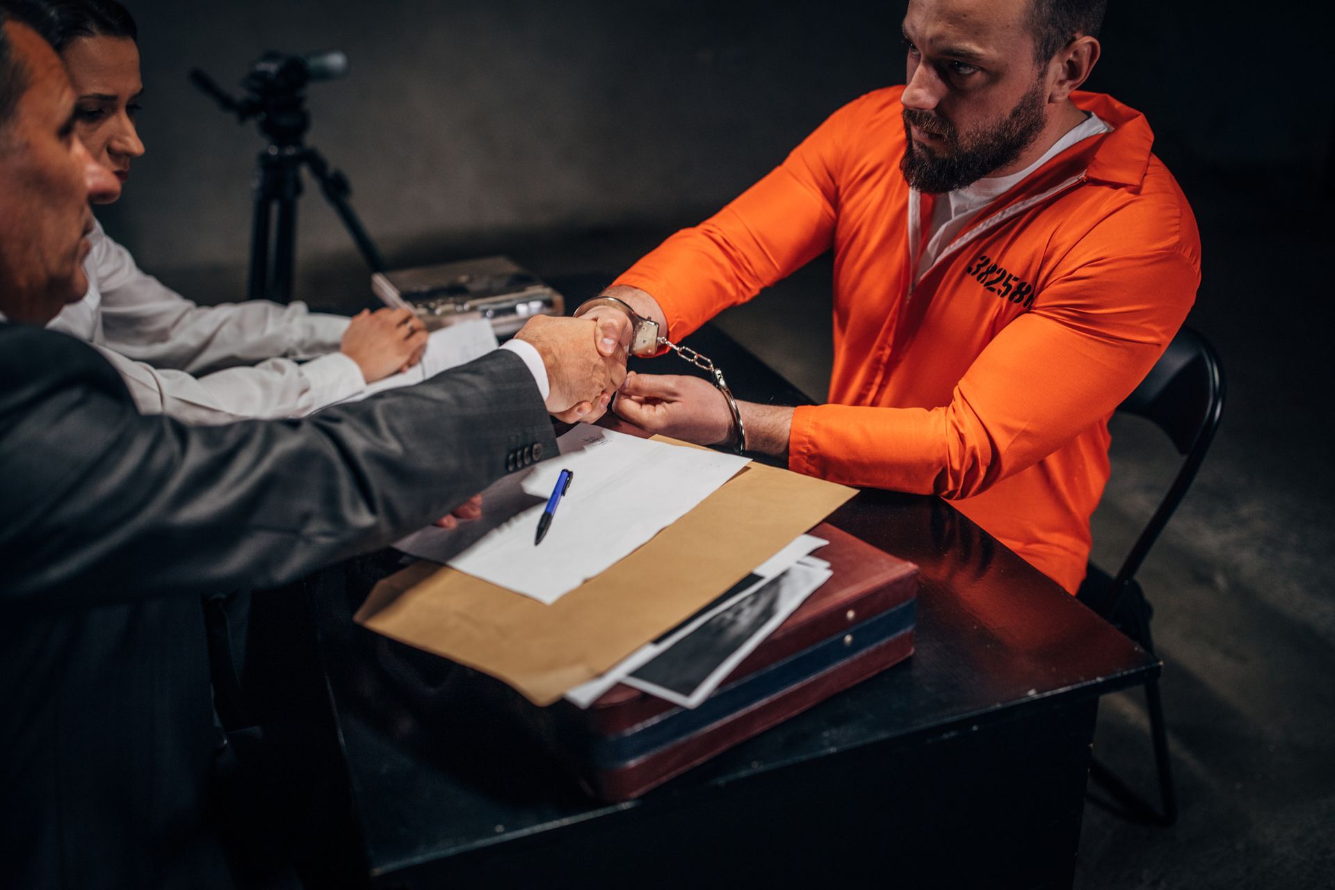Man with handcuffs and two detectives/lawyer sitting in the investigation room