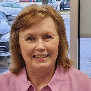 A woman in a pink shirt is smiling for the camera.