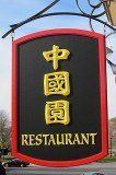 A restaurant sign with chinese characters on it is hanging from a pole.