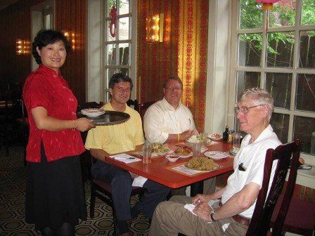 A woman in a red shirt is serving a tray of food to three men sitting at a table