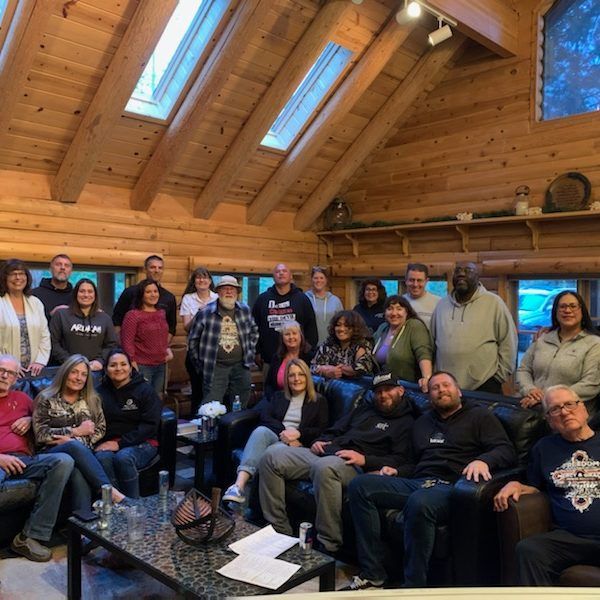 Group of people in a wood-paneled cabin; some seated, others standing.