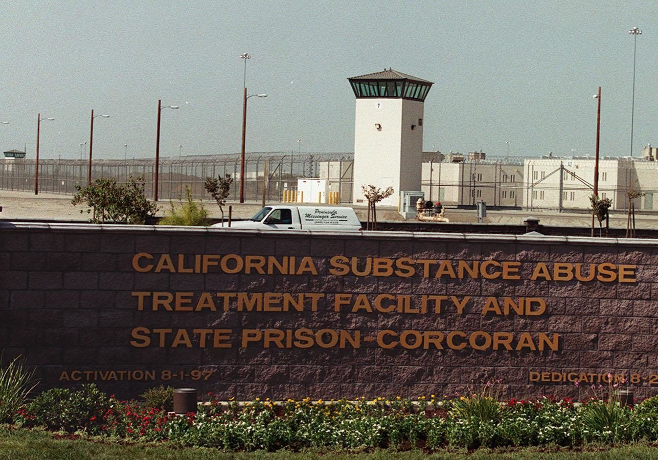 California Substance Abuse Treatment Facility and State Prison-Corcoran sign with guard tower and fences in the background.
