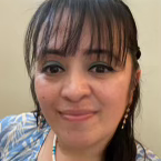 Woman with dark hair and bangs, smiling, wearing blue shirt and earrings.