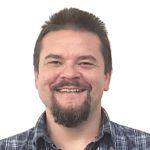 Man with beard and smiling, wearing a blue plaid shirt.