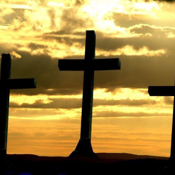 Three dark crosses silhouetted against a golden sunset with cloudy sky.