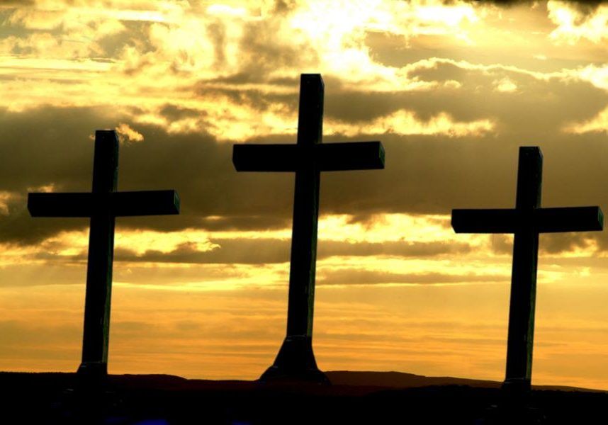 Three dark crosses silhouetted against a golden sunset sky.