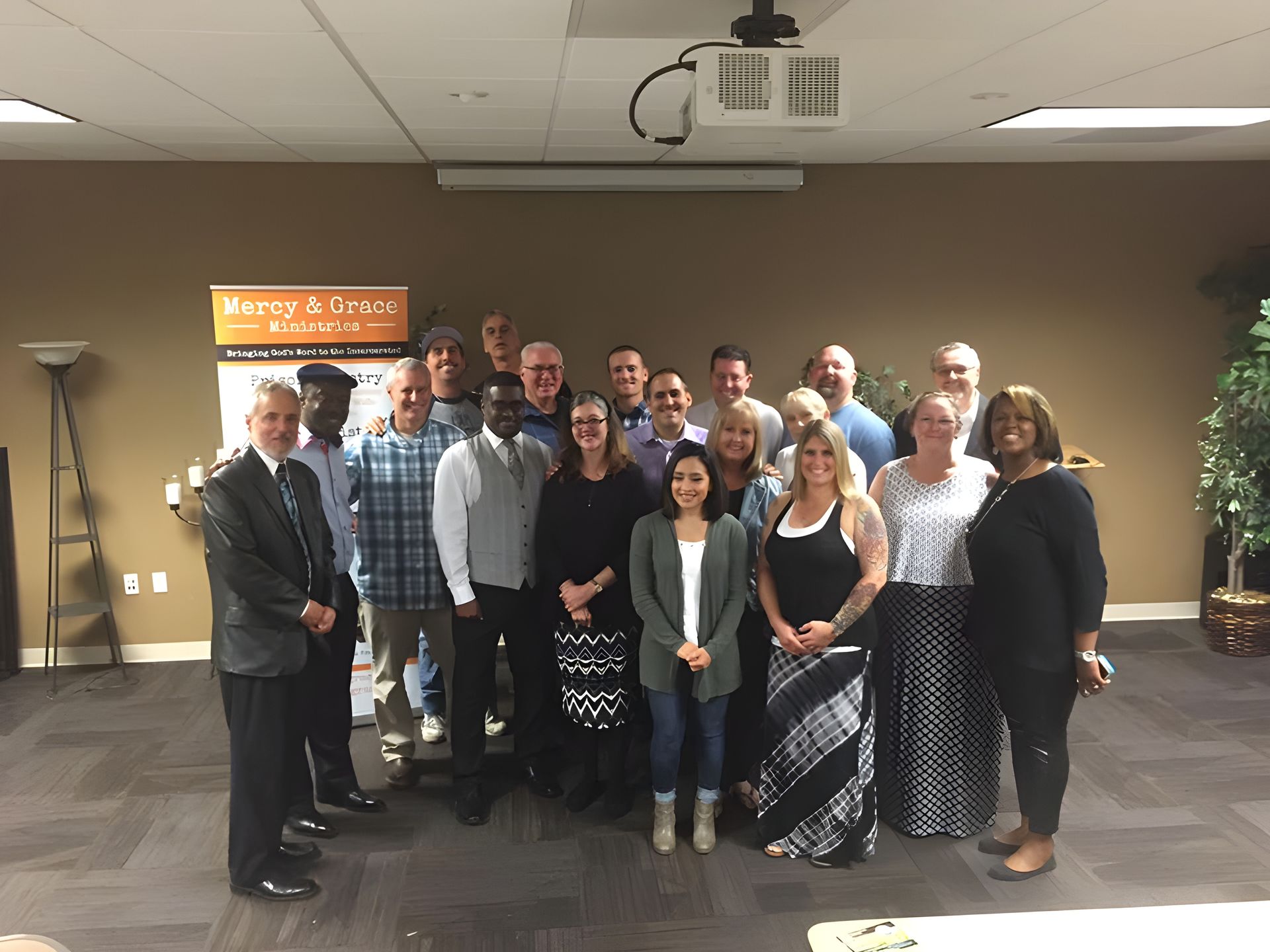 Group of people in a meeting room, posing for a photo. Beige walls, projector on the ceiling.