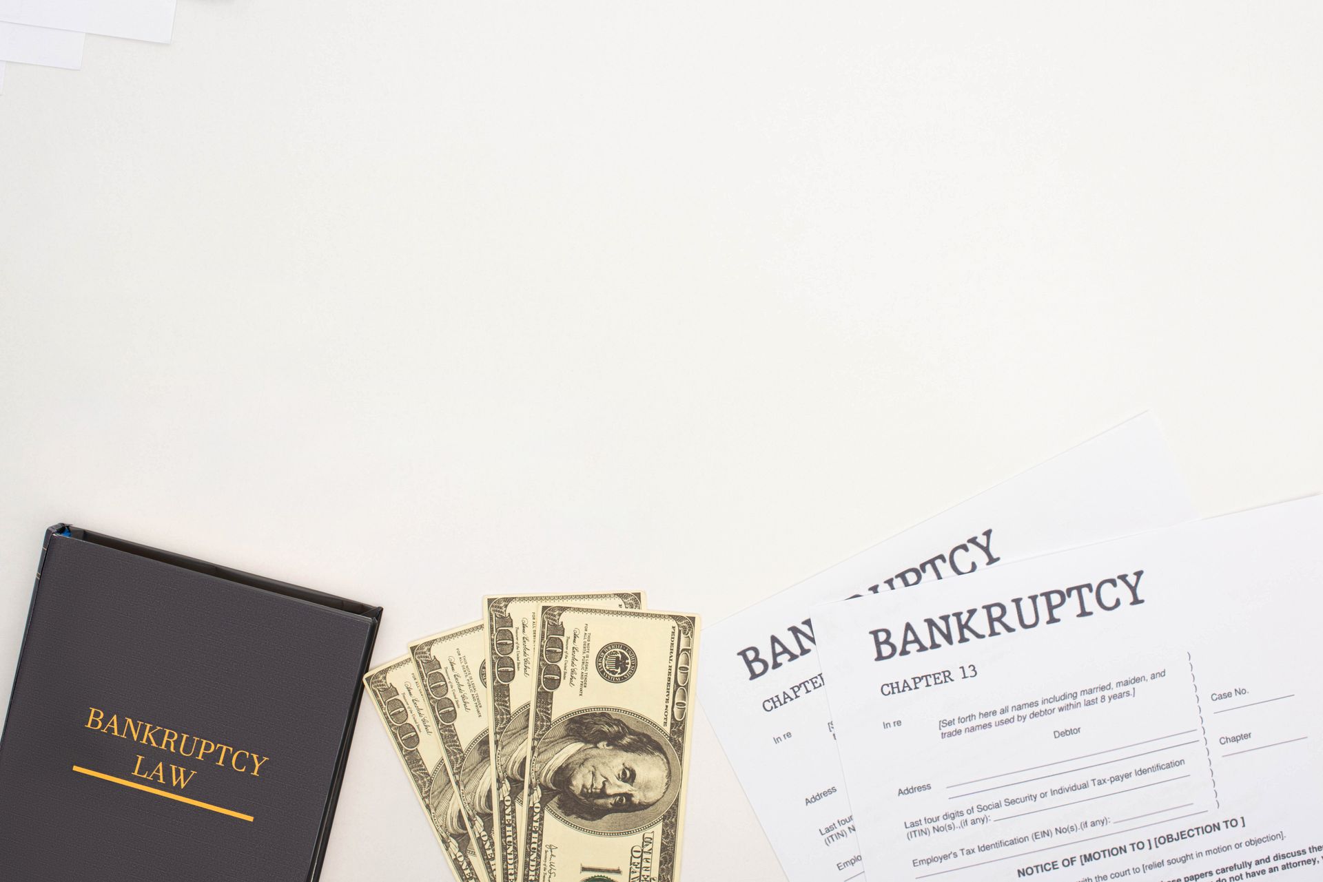 Black law book and cash next to bankruptcy forms, on a white surface.