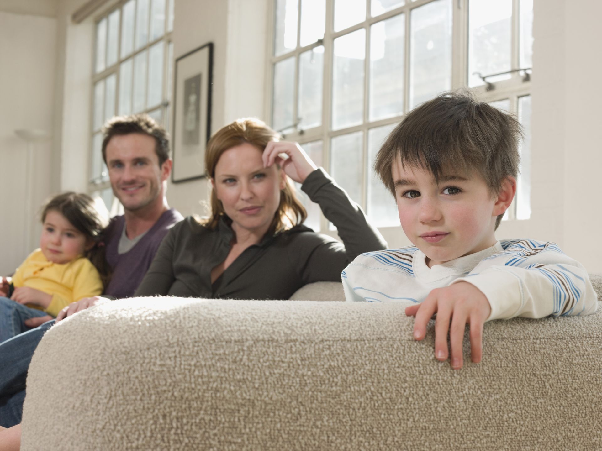 Family of four on a couch; boy in foreground, looking at viewer. Representing child custody