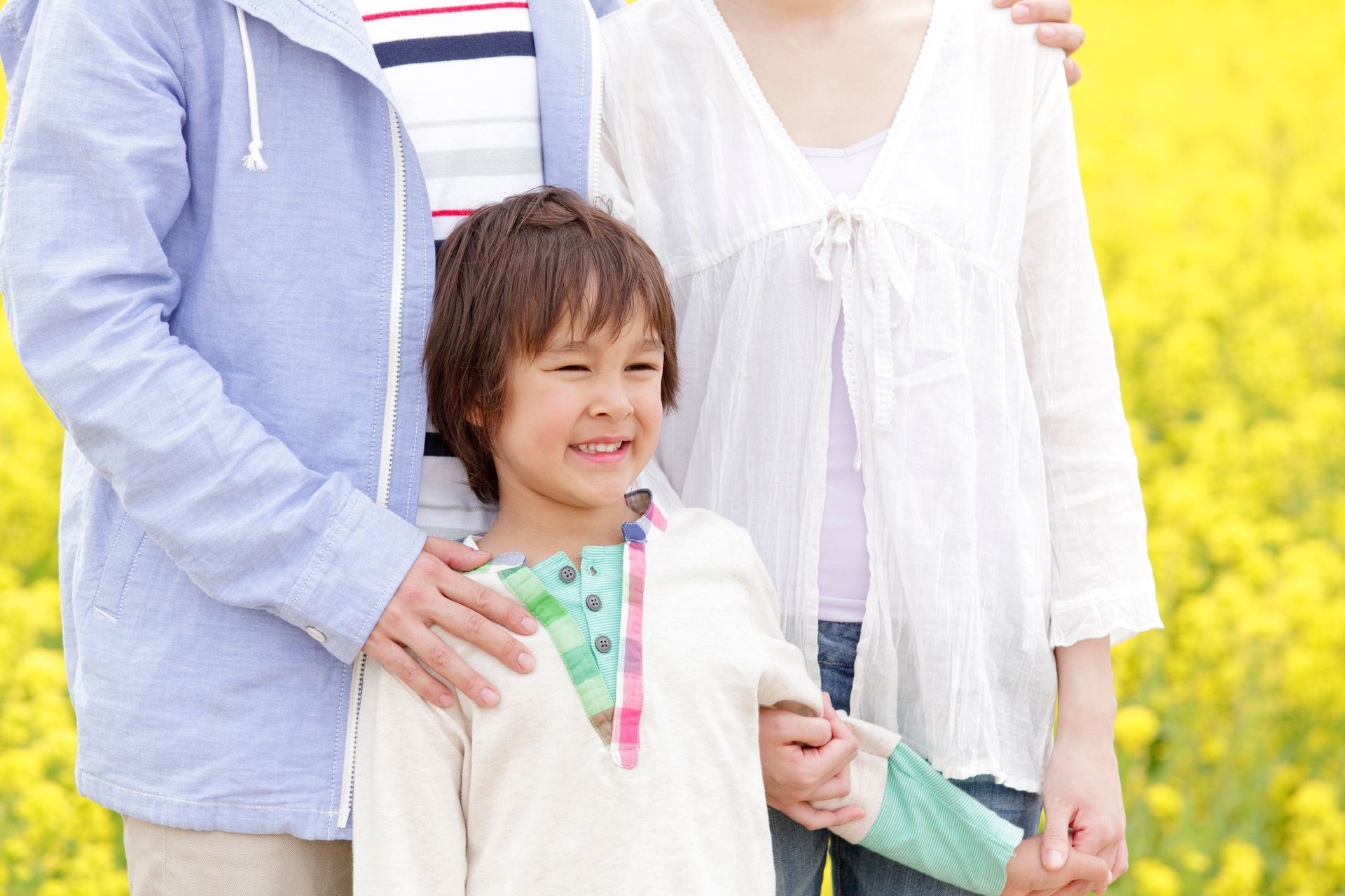 Family of three in a field of yellow flowers; child smiles, parents have arms around them.