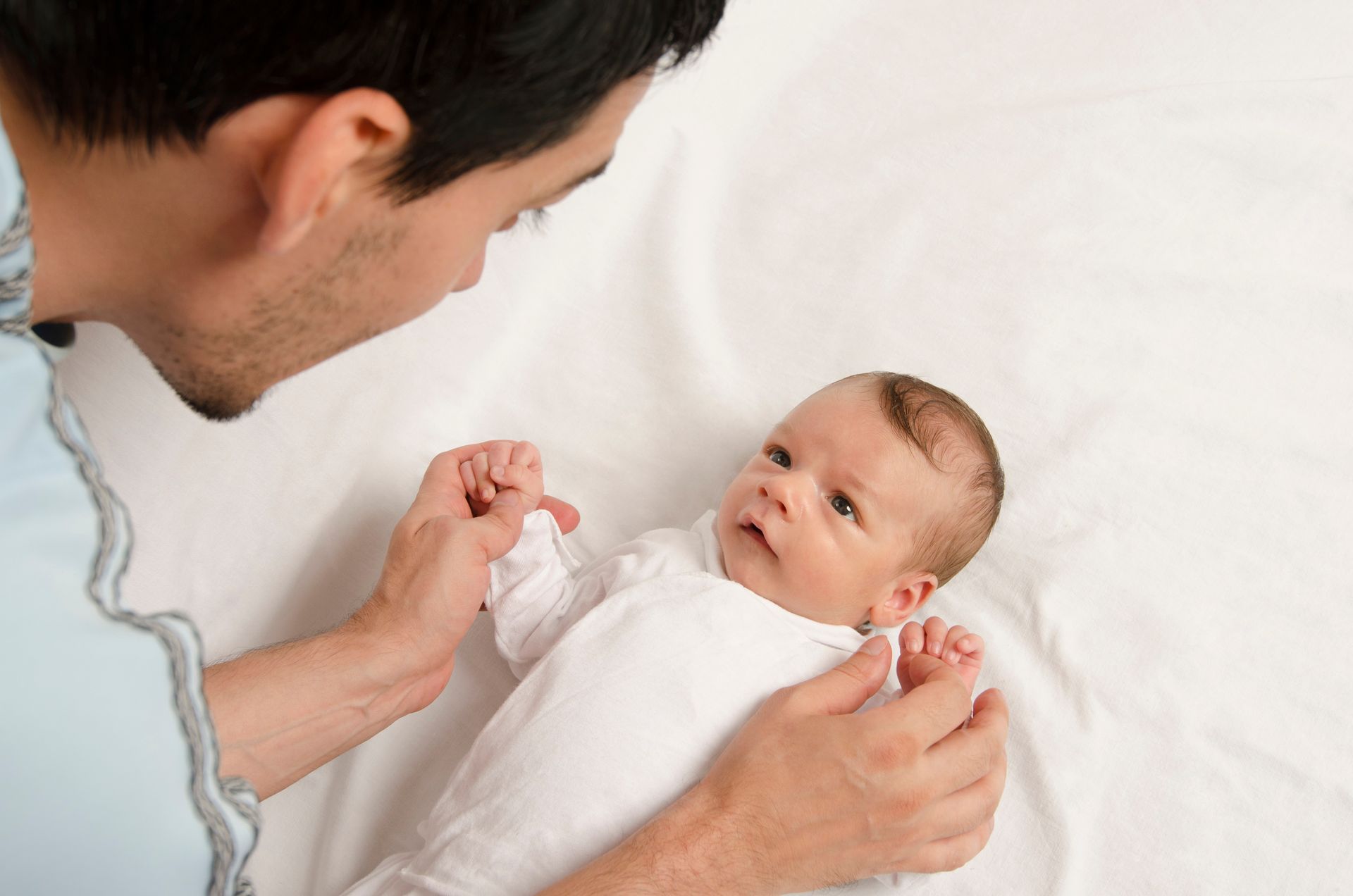 Father looking at a newborn baby lying on a white sheet.