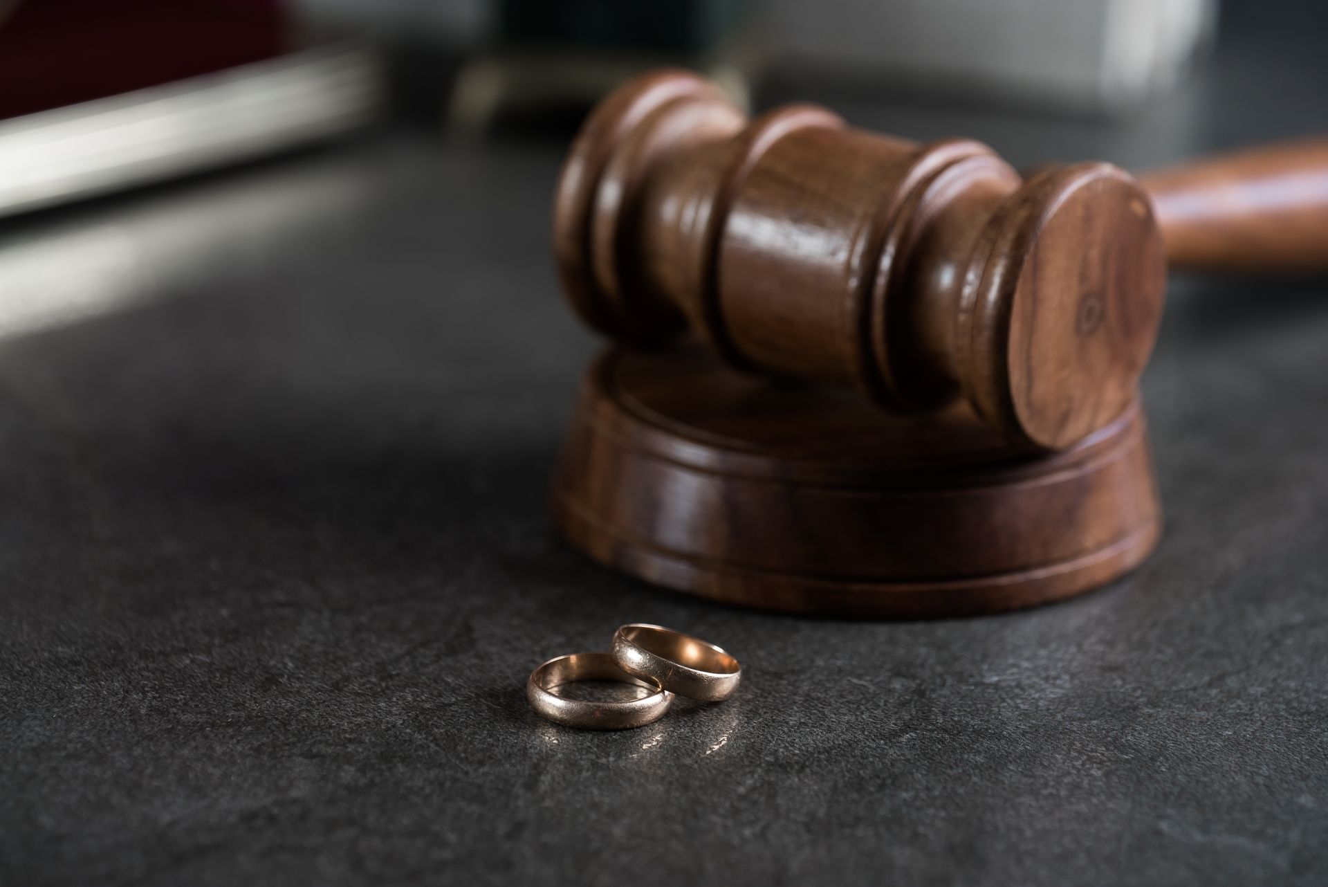 Wedding rings near a gavel on a dark surface, symbolizing divorce or legal proceedings.