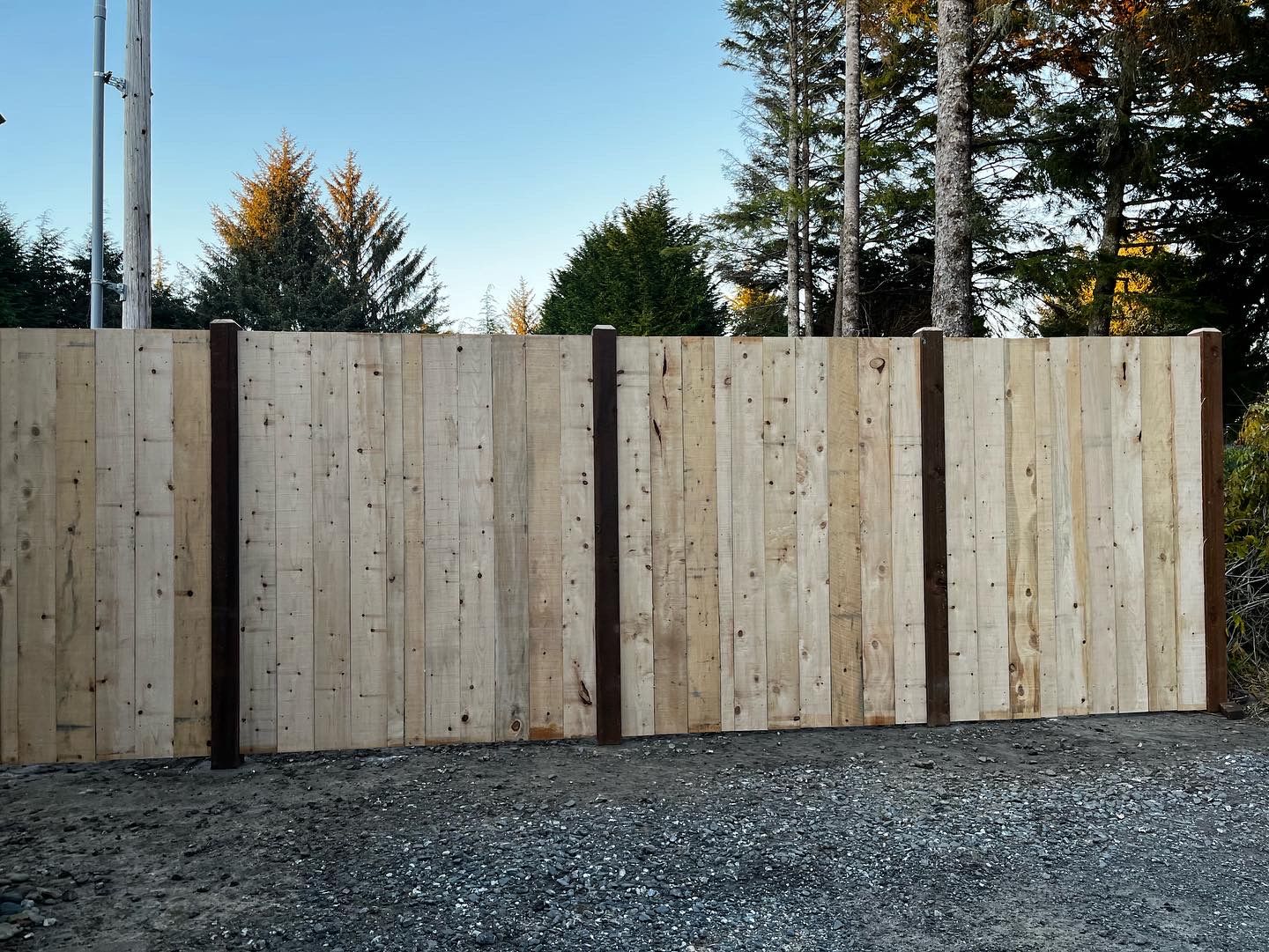 A wooden fence is surrounded by gravel and trees