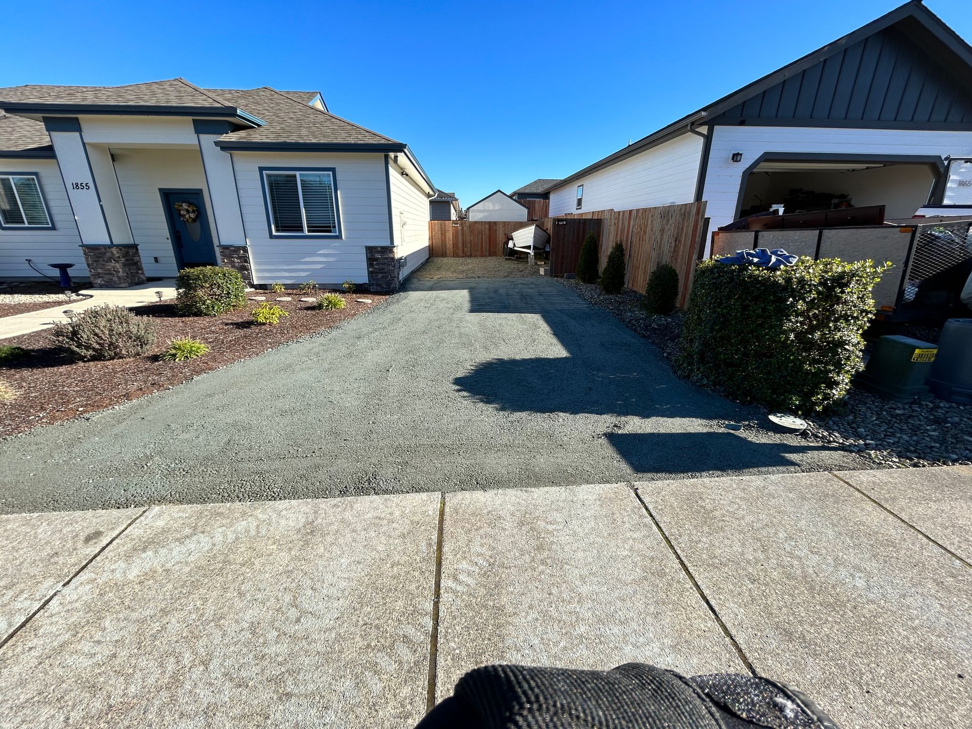 A person is standing in front of a house with a gravel driveway leading to it.