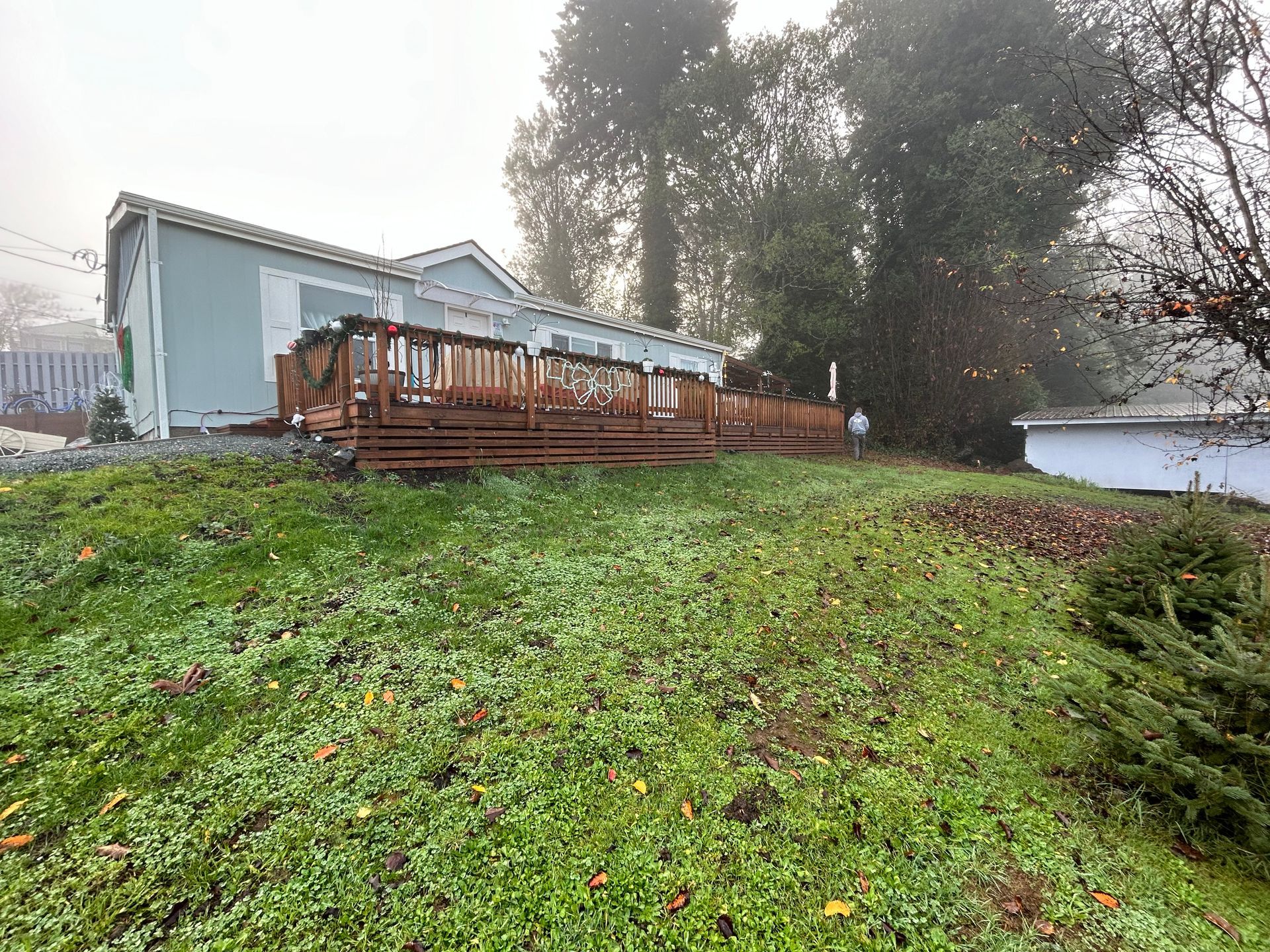 A house with a large deck is sitting on top of a grassy hill.