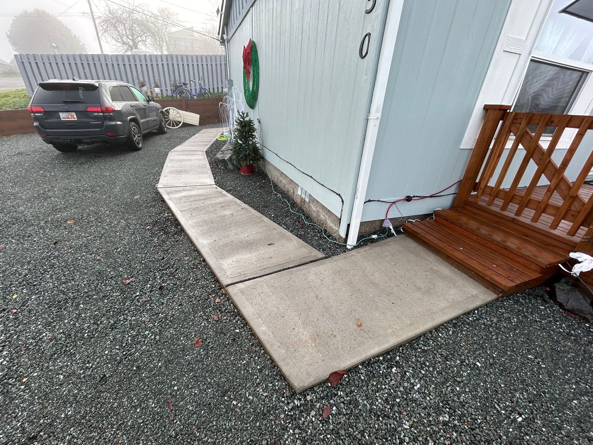 A car is parked on the side of a house next to a sidewalk.