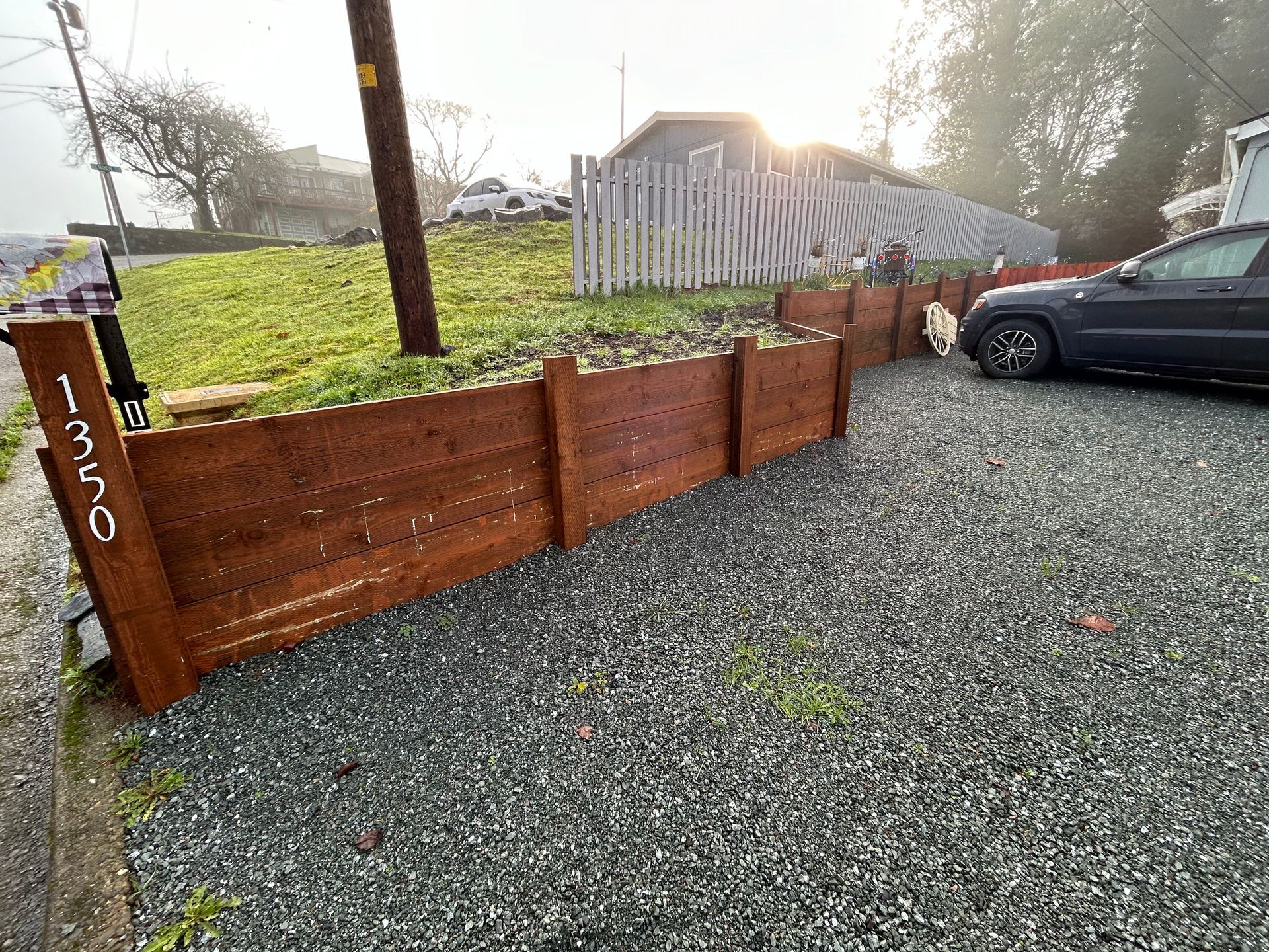 A car is parked in a gravel lot next to a wooden fence.