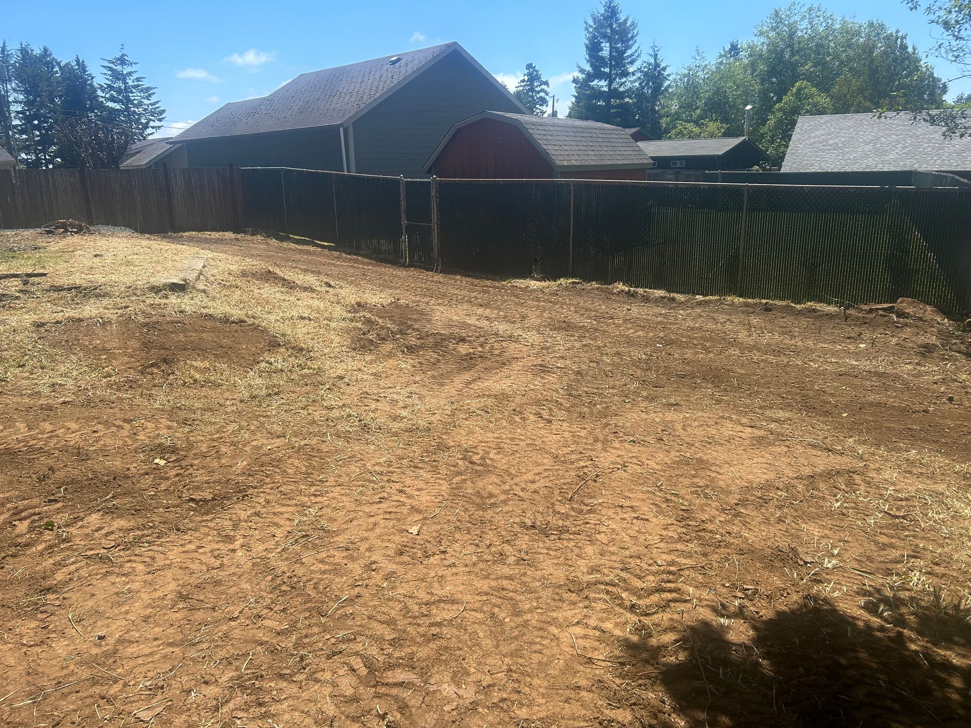 A dirt field with a fence and a house in the background
