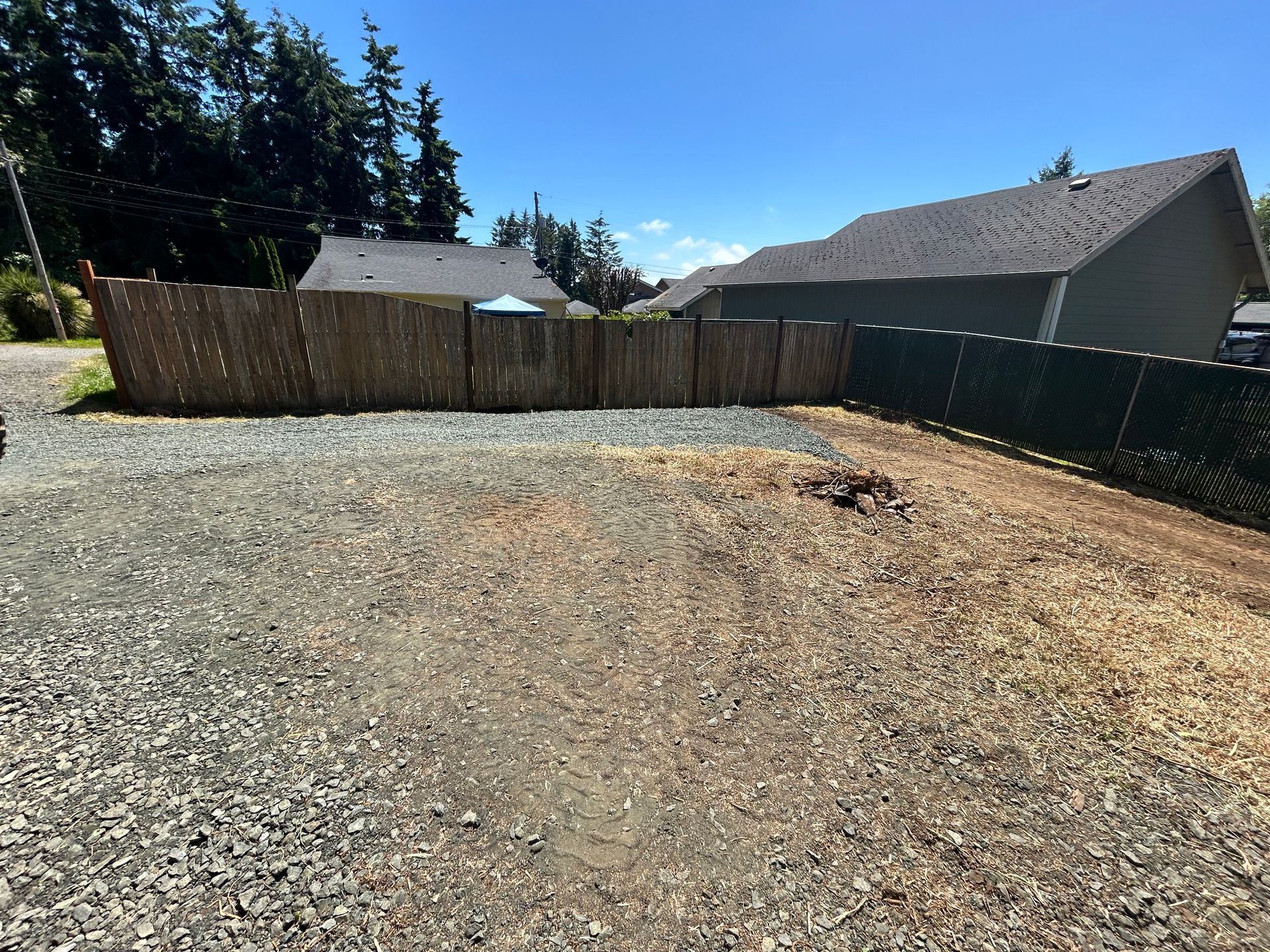 A gravel area with a fence and a house in the background