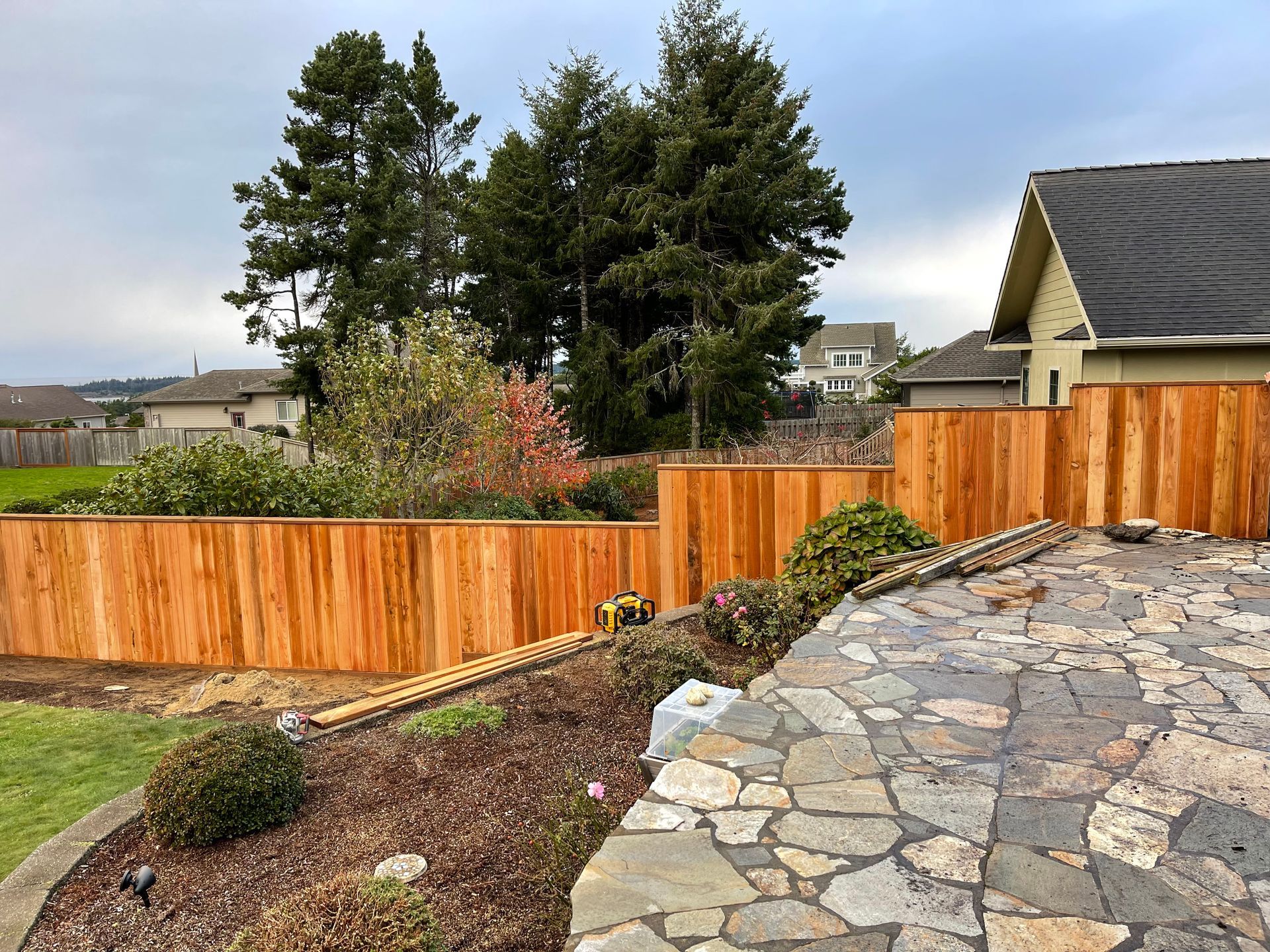 A wooden fence surrounds a stone walkway in front of a house.