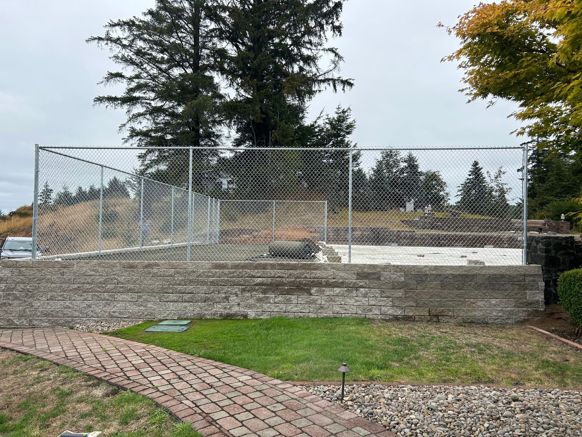 A chain link fence is surrounding a basketball court in a backyard.