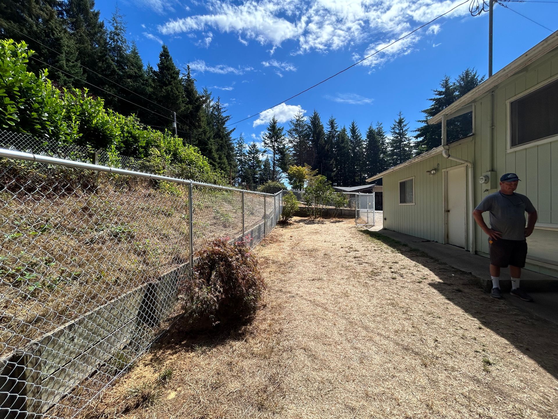A man is standing in front of a chain link fence next to a house.