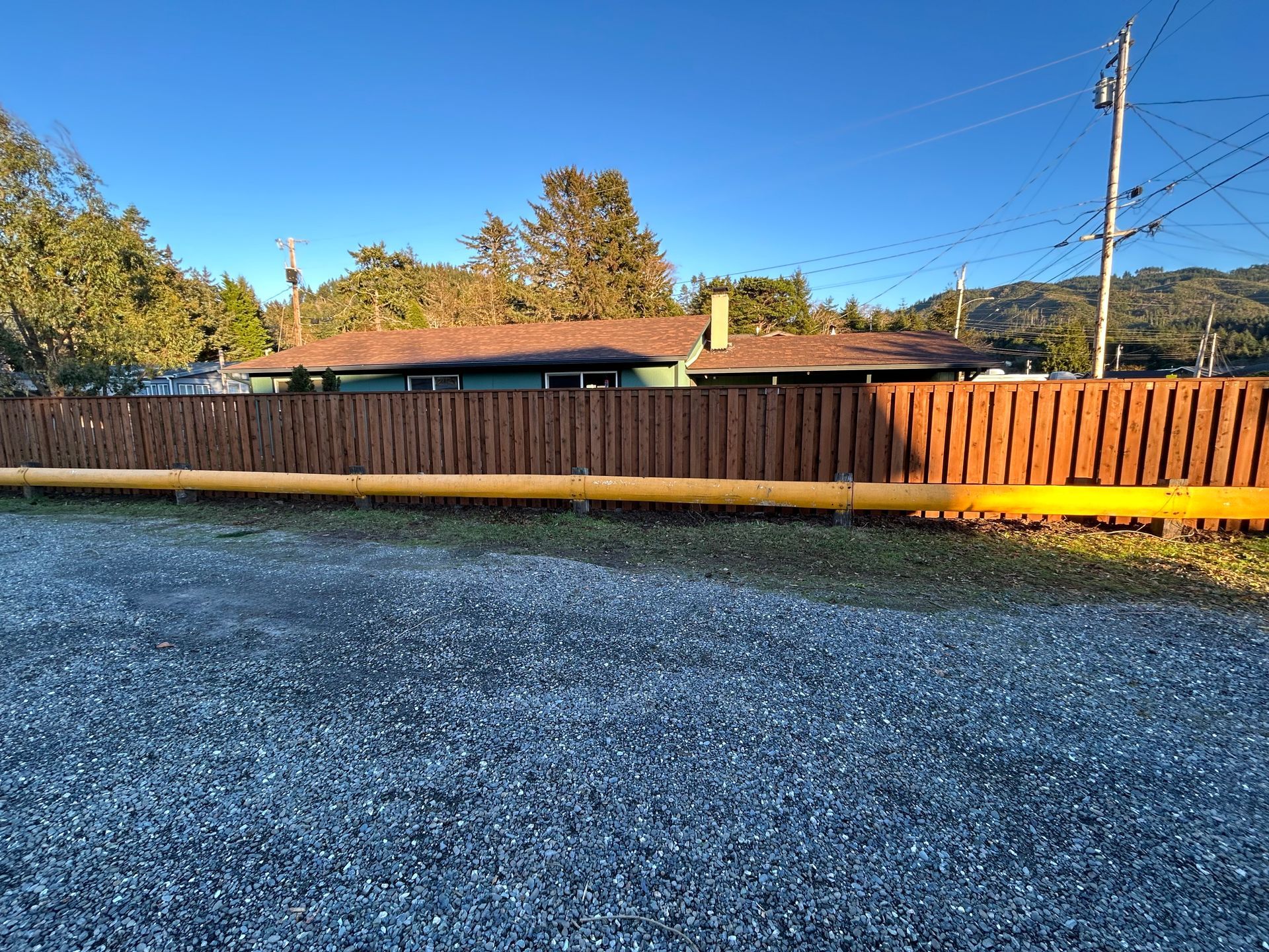 A wooden fence surrounds a gravel driveway in front of a house.