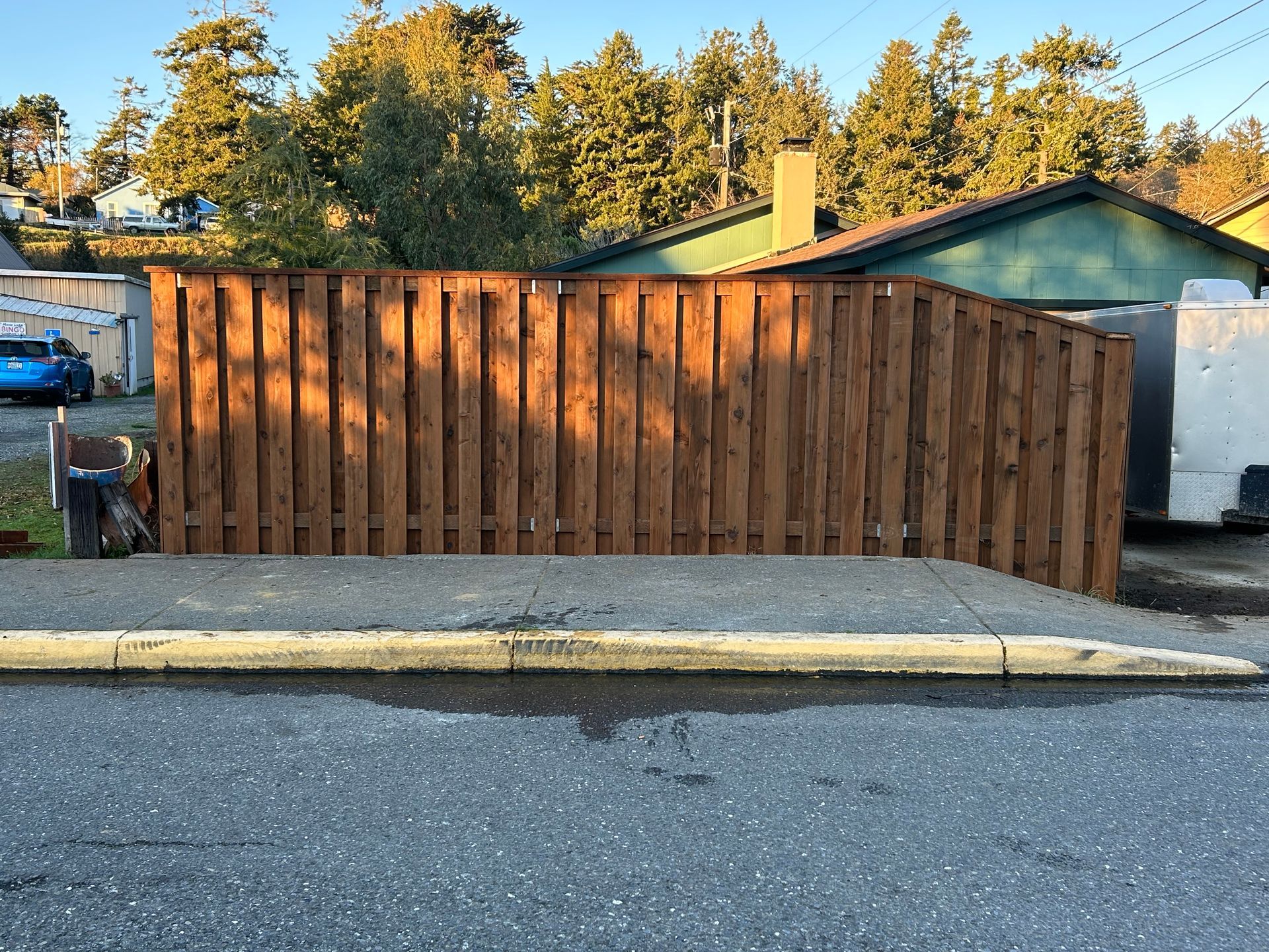 A wooden fence is sitting on the side of the road in front of a house.