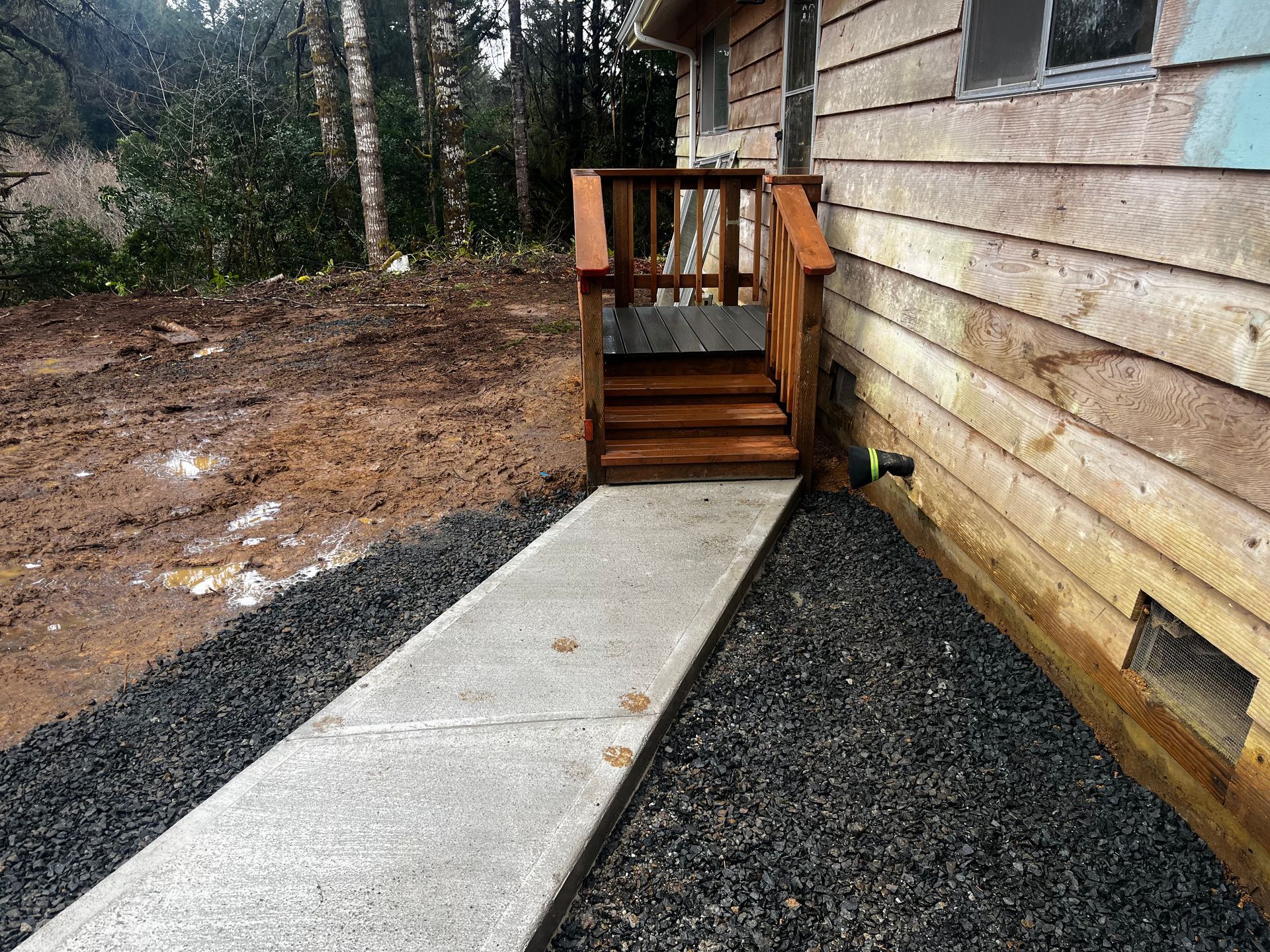 A concrete walkway leading to a wooden deck on the side of a house.