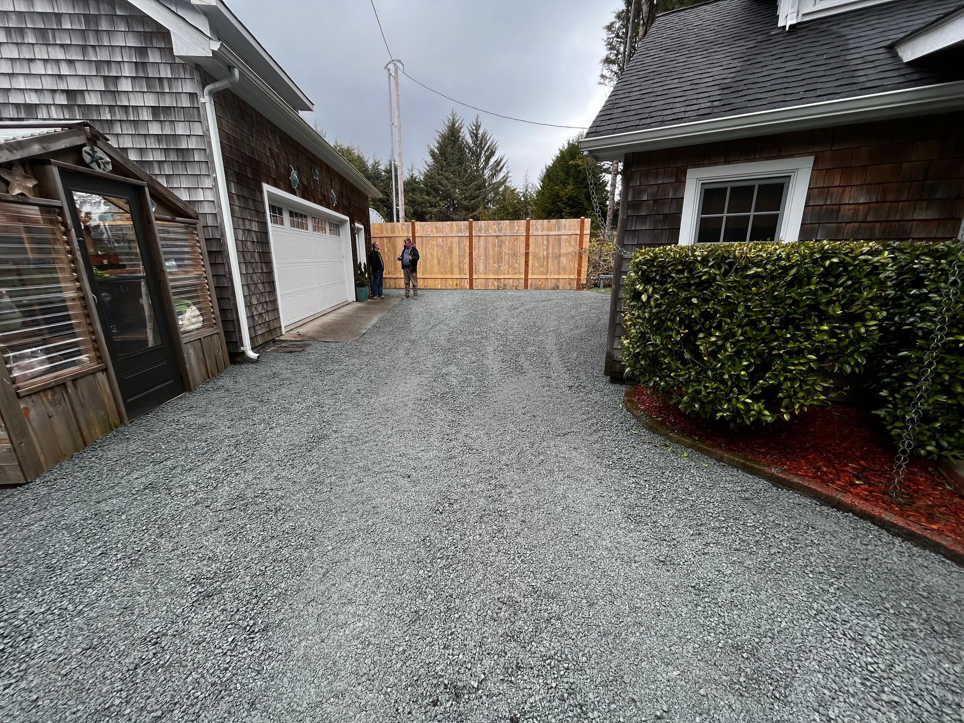 A gravel driveway leading to a house with a wooden fence.