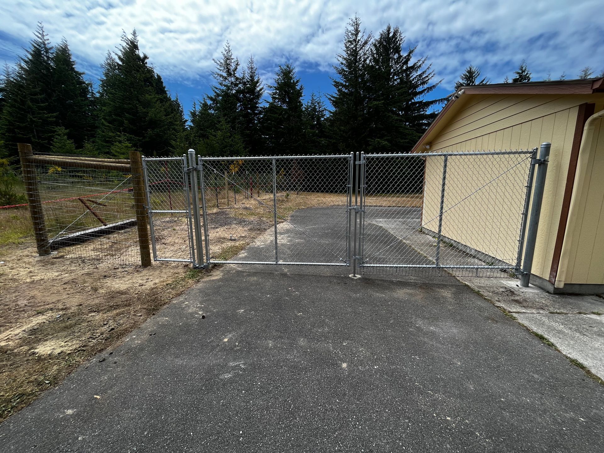 A chain link fence surrounds a driveway leading to a garage.
