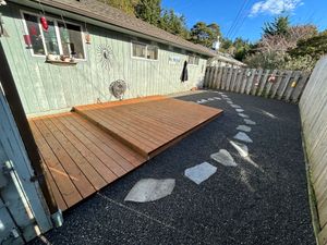 Backyard with a small wooden deck beside a shed, gravel ground, and a fenced perimeter.