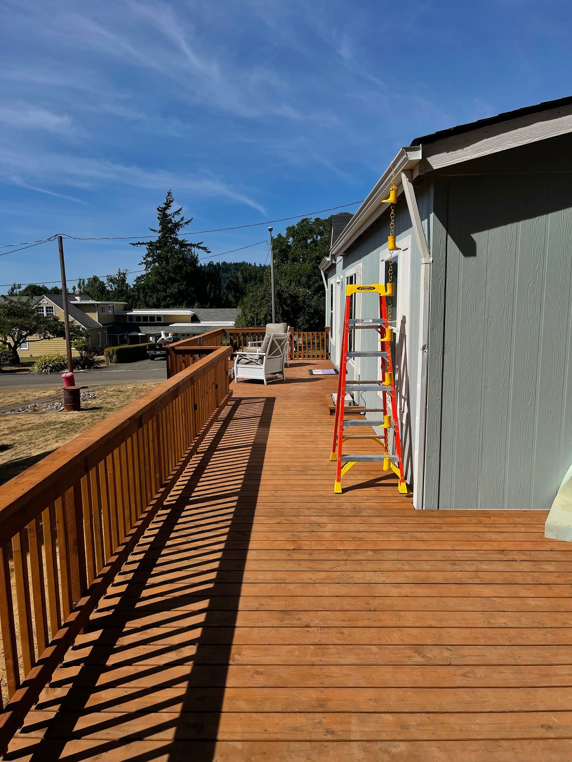 A ladder is sitting on a wooden deck next to a house.