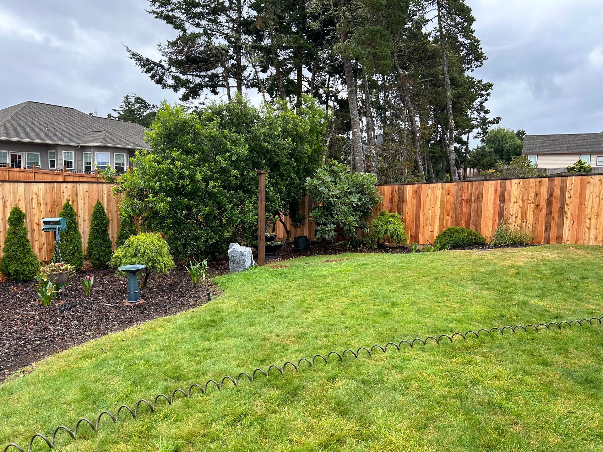 A backyard with a wooden fence and a lush green lawn.