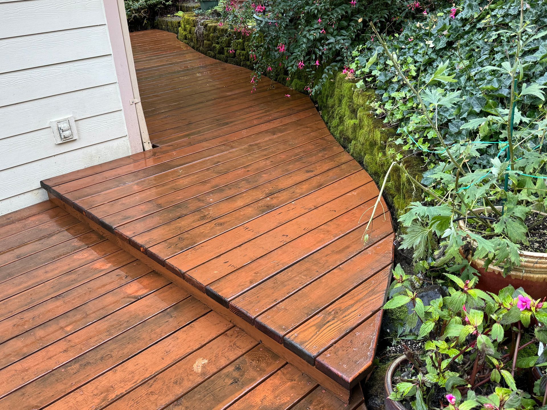 A wooden walkway leading to a house with flowers in the background.