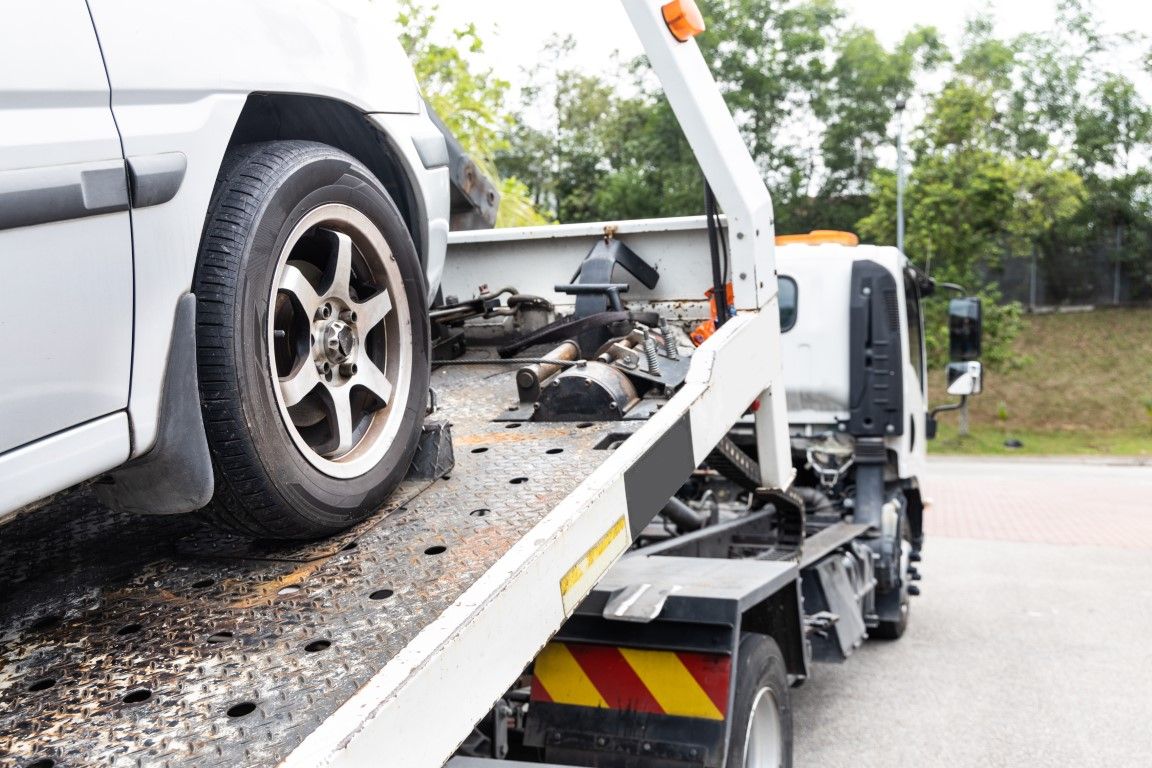 White car being towed by a tow truck on a paved road.