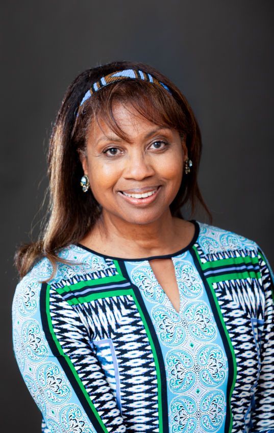 A woman in a blue and green shirt is smiling for the camera.