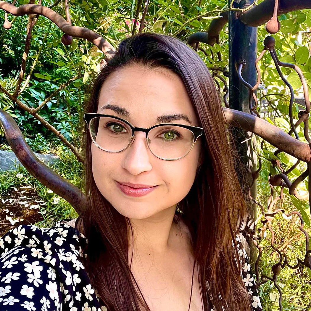 a woman wearing glasses is standing in front of a tree .