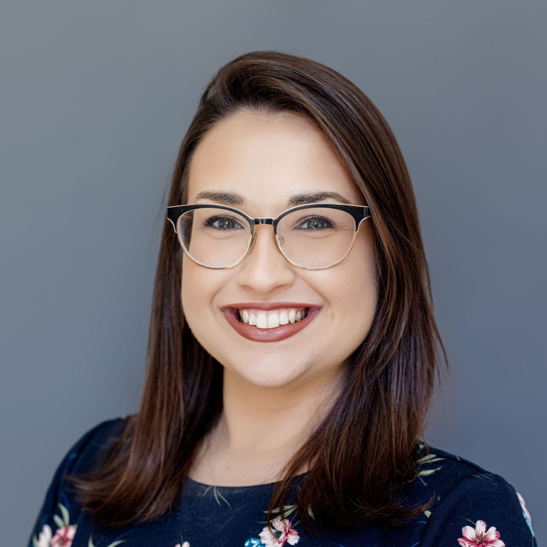 A woman wearing glasses and a floral shirt is smiling for the camera.