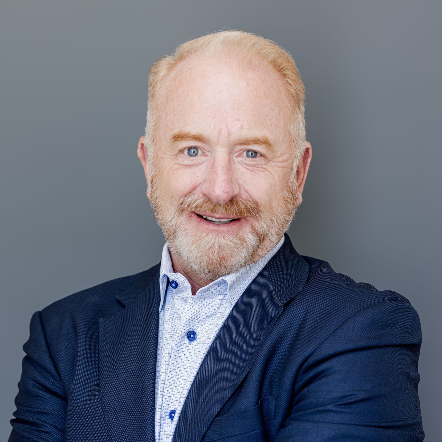 A man with a beard is wearing a blue suit and smiling.