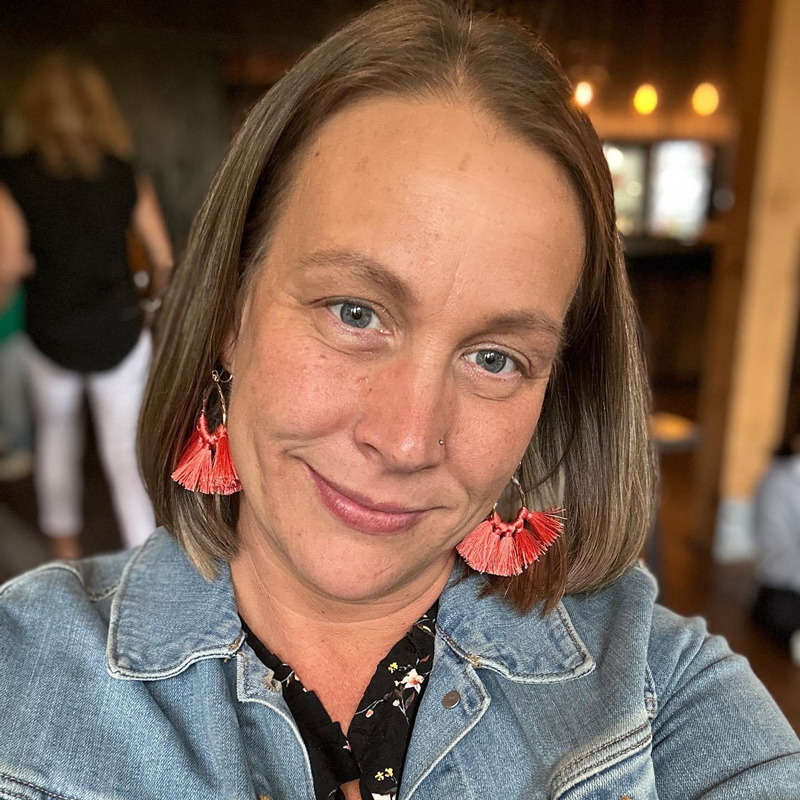 a woman wearing a denim jacket and earrings is smiling for the camera .