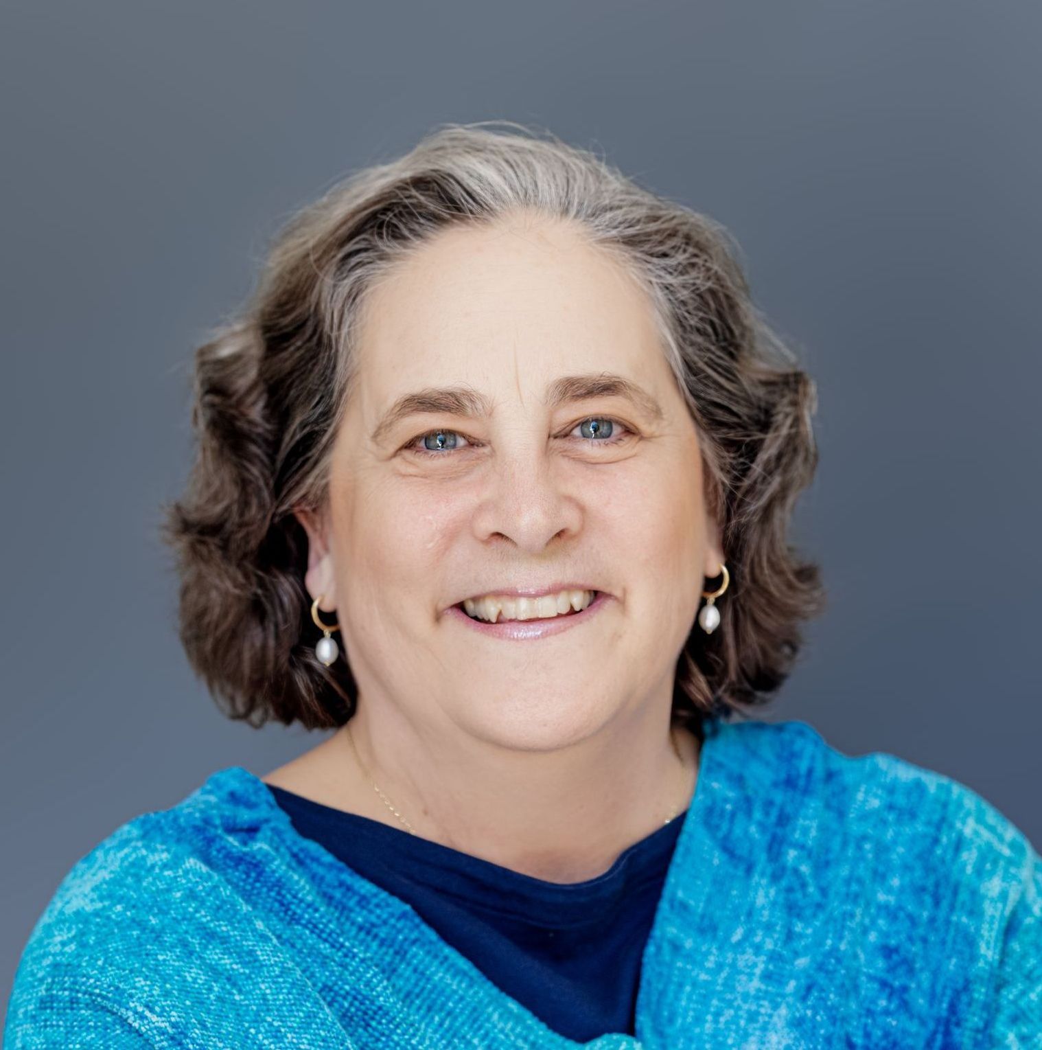 A woman wearing a blue sweater and earrings smiles for the camera