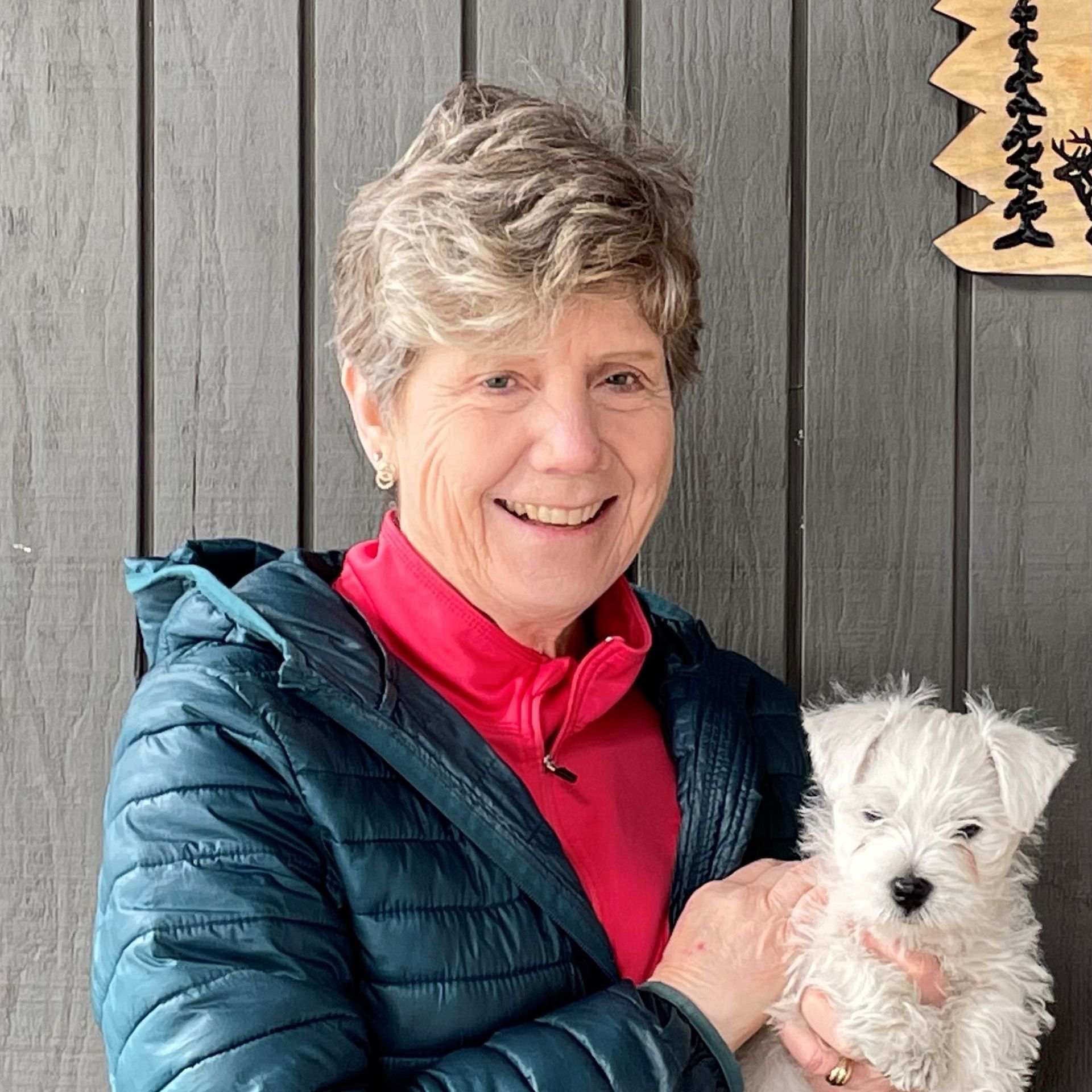 A woman in a blue jacket is holding a small white dog.