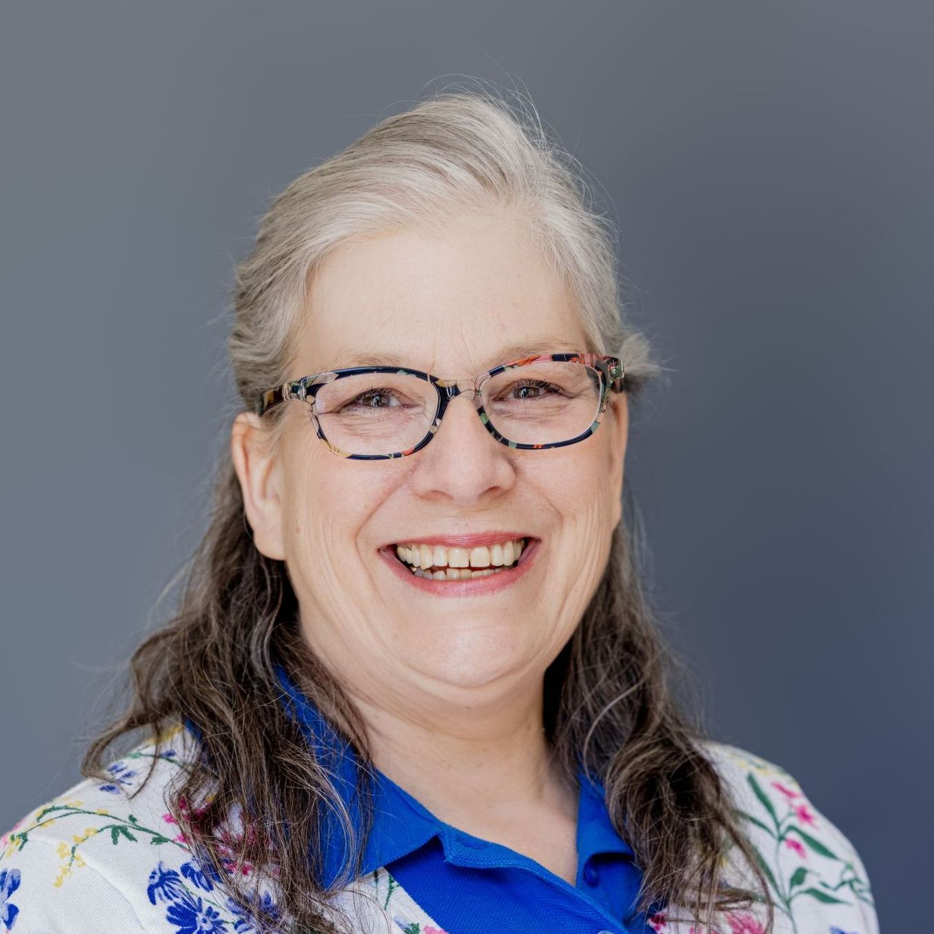 A woman wearing glasses and a blue shirt is smiling for the camera.