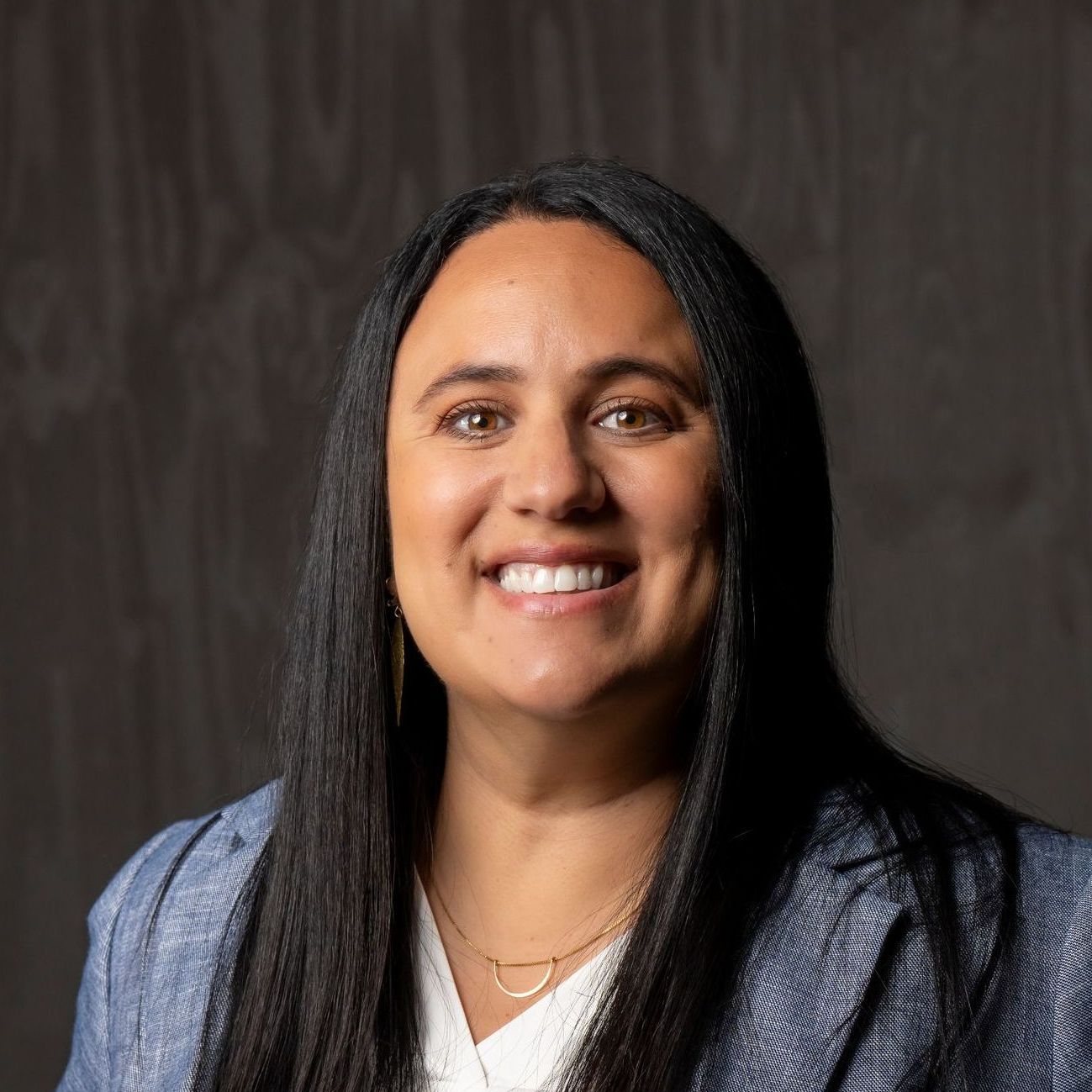 A woman with long black hair and a blue jacket is smiling for the camera.