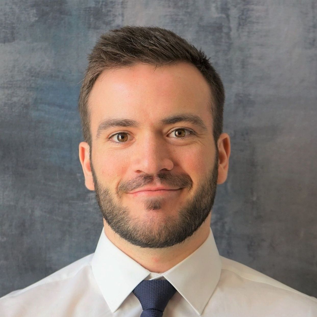 A man with a beard wearing a white shirt and blue tie