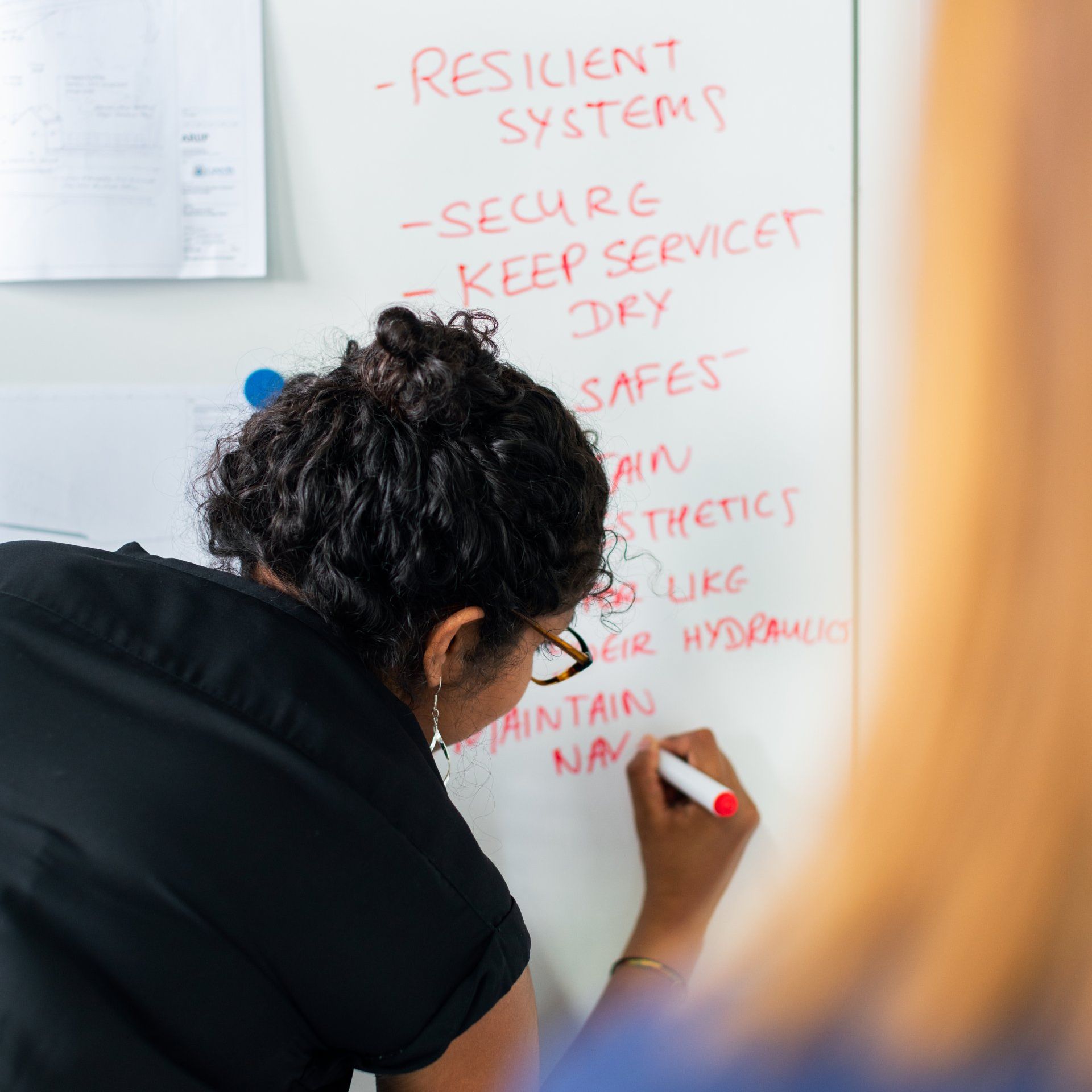 a woman is writing on a white board that says resilient systems